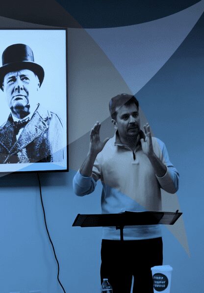Man giving a speech in front of a Lincoln portrait.