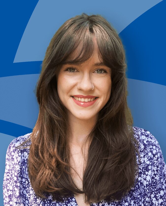 A young woman with long brown hair smiling against a blue background.