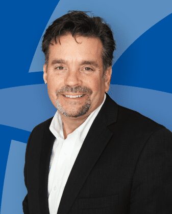 A smiling man in a black blazer against a blue background.
