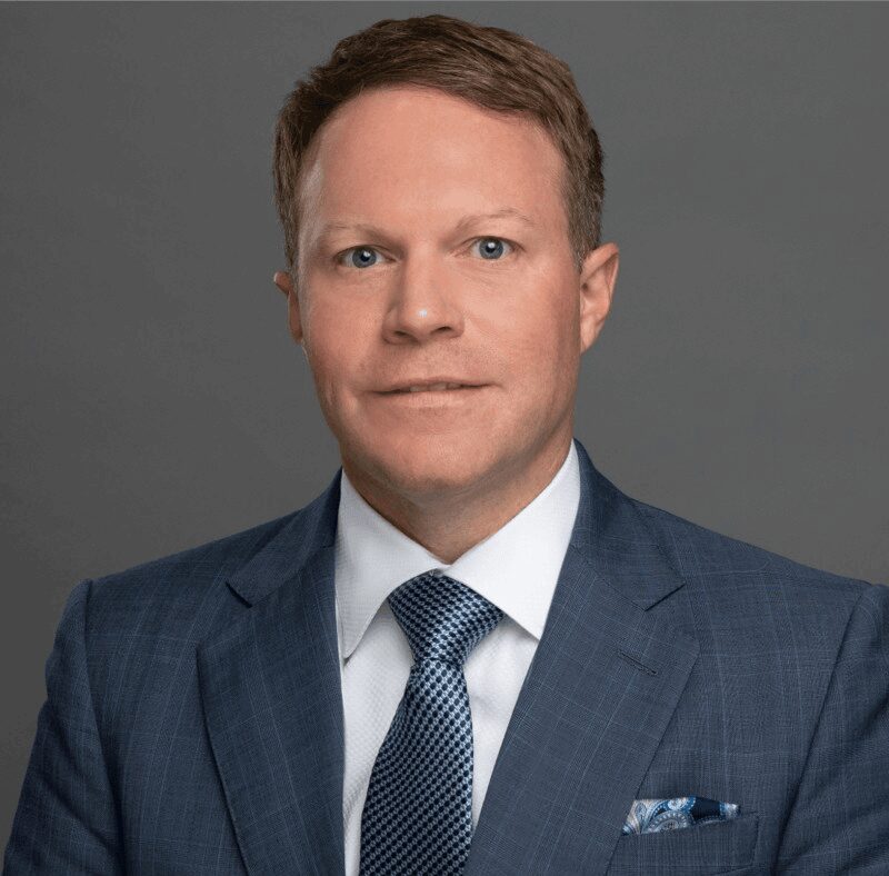 Professional man in a blue suit and tie posing against a gray background.
