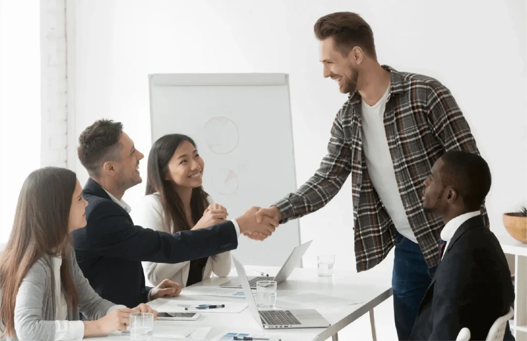 Three colleagues shaking hands in a meeting room, smiling